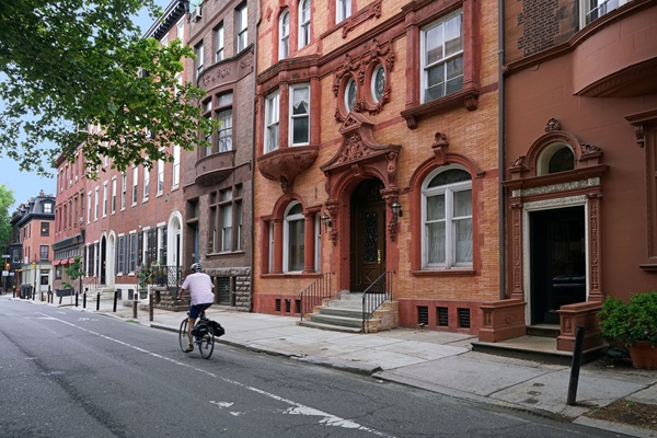 Cyclist riding in a designated bike lane along a historic brick street lined with brownstone buildings in Boston.