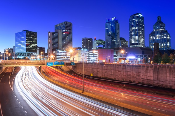 A multi-lane highway in Hartford, Connecticut, featuring an illuminated skyline, with white and red light trails from passing vehicles under a dark blue sky.