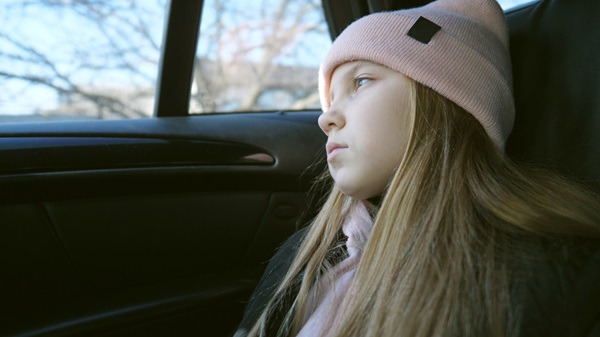 A young girl wearing a pink winter hat looking thoughtfully out of a car window, depicting a child potentially suffering from the quiet symptoms of a traumatic brain injury.