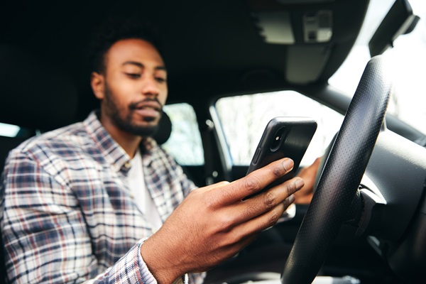 A man in a plaid shirt distracted by his smartphone while behind the wheel of a car, a leading cause of texting and driving crashes across Massachusetts.