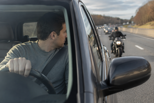 A driver looking over his shoulder while a motorcyclist follows behind on a highway, illustrating the dangerous visibility issues and blind spots that contribute to Connecticut motorcycle crash fatality risks.